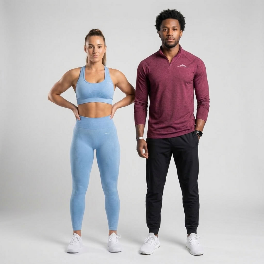 A man and a woman modeling activewear in a studio setting. The woman wears a light blue sports bra and matching high-waisted leggings, while the man wears a heathered maroon long-sleeve quarter-zip pullover, black joggers, and white sneakers.